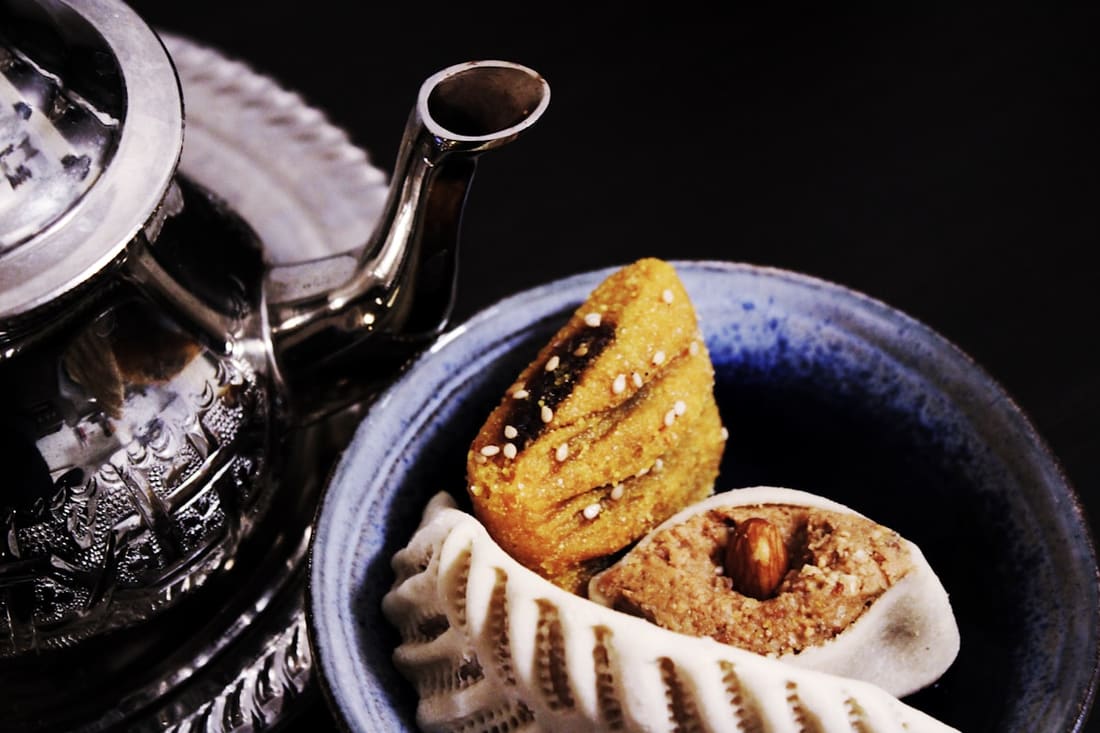 Teiera marocchina in metallo martellato accanto a una ciotola di dolci alle mandorle
