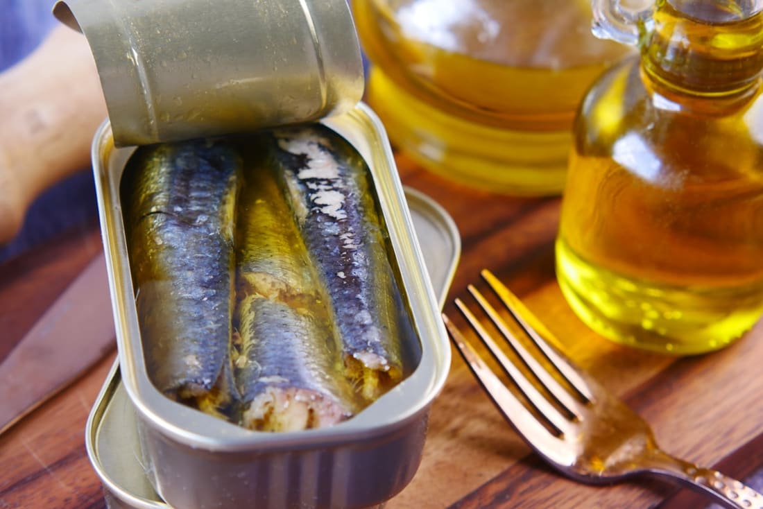 Latta di sardine aperta con filetti sott’olio, forchetta e ampolla d’olio